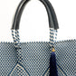 Closeup of fabric of blue and white chevron woven bucket bag made from recycled plastics featuring navy blue leather handles and tassel detail