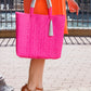 Woman wearing orange dress and brown heels holding a hot pink woven bucket bag in a city setting