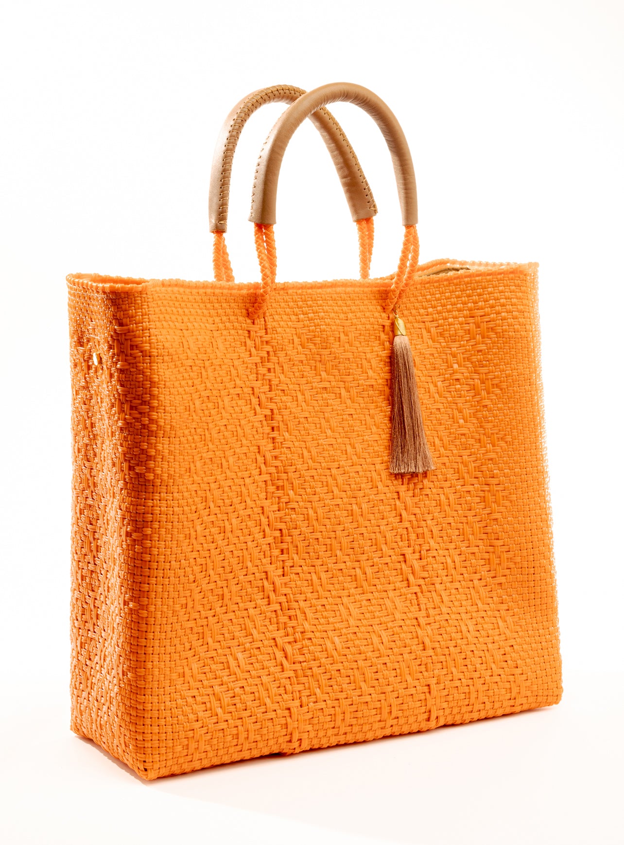 Side angle of orange woven tote bag made from recycled plastics with tan handles and tan tassel detail