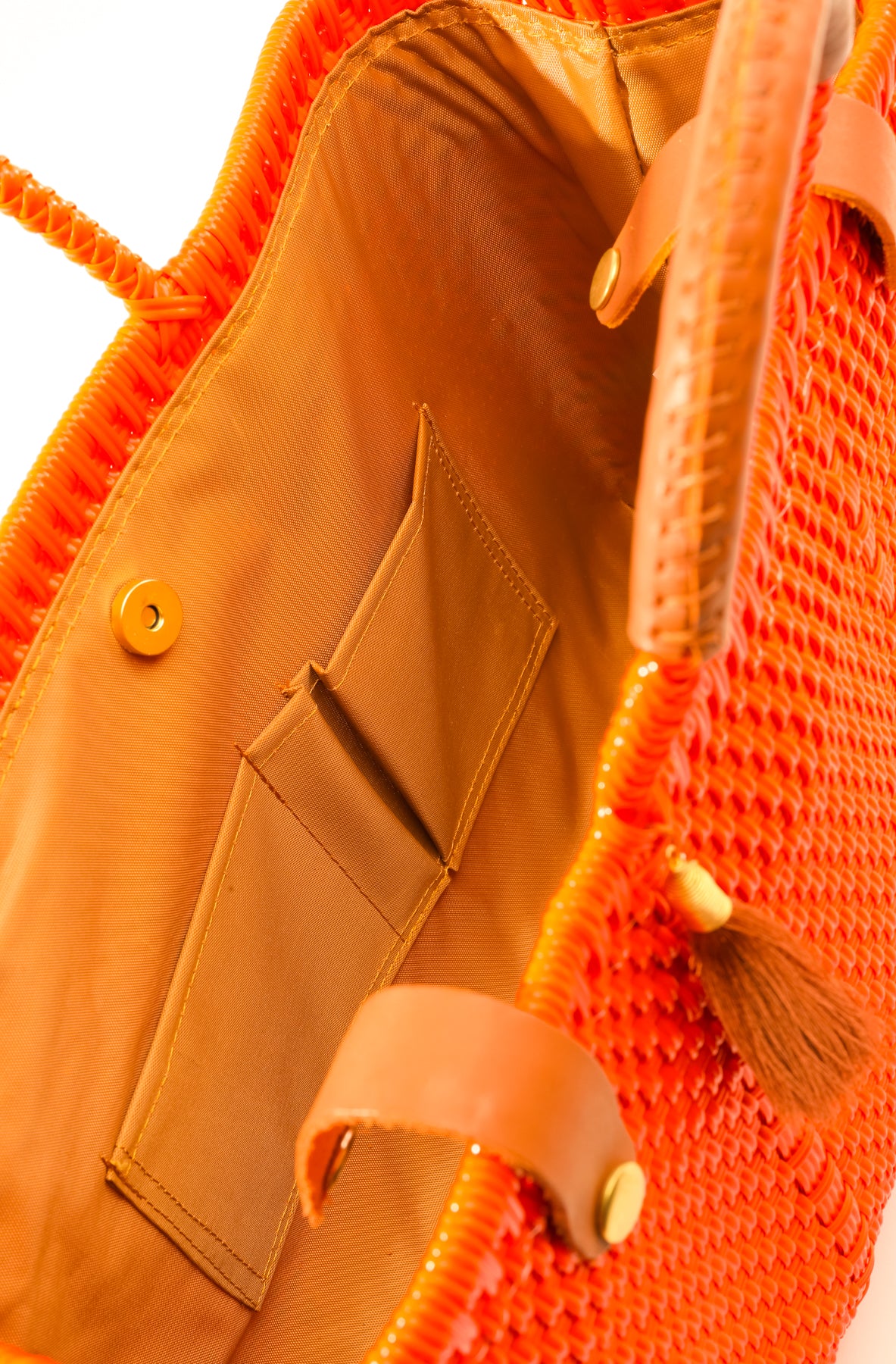 Inside tan lining, pockets, and magnetic closure of orange woven handbag with tan leather handle, closure straps, and tassel