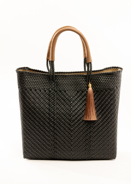 Black and brown woven bucket bag made from recycled plastics featuring tan leather handles and tassel detail