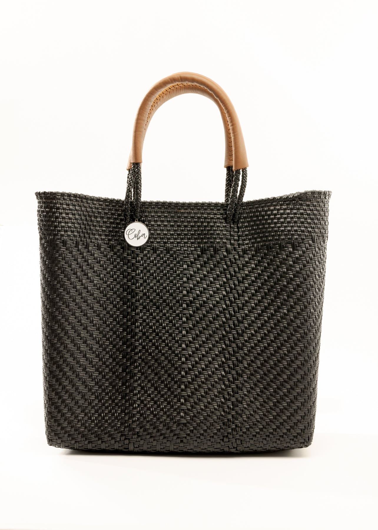 Black and brown woven bucket bag made from recycled plastics featuring tan leather handles and a silver Coba logo medallion