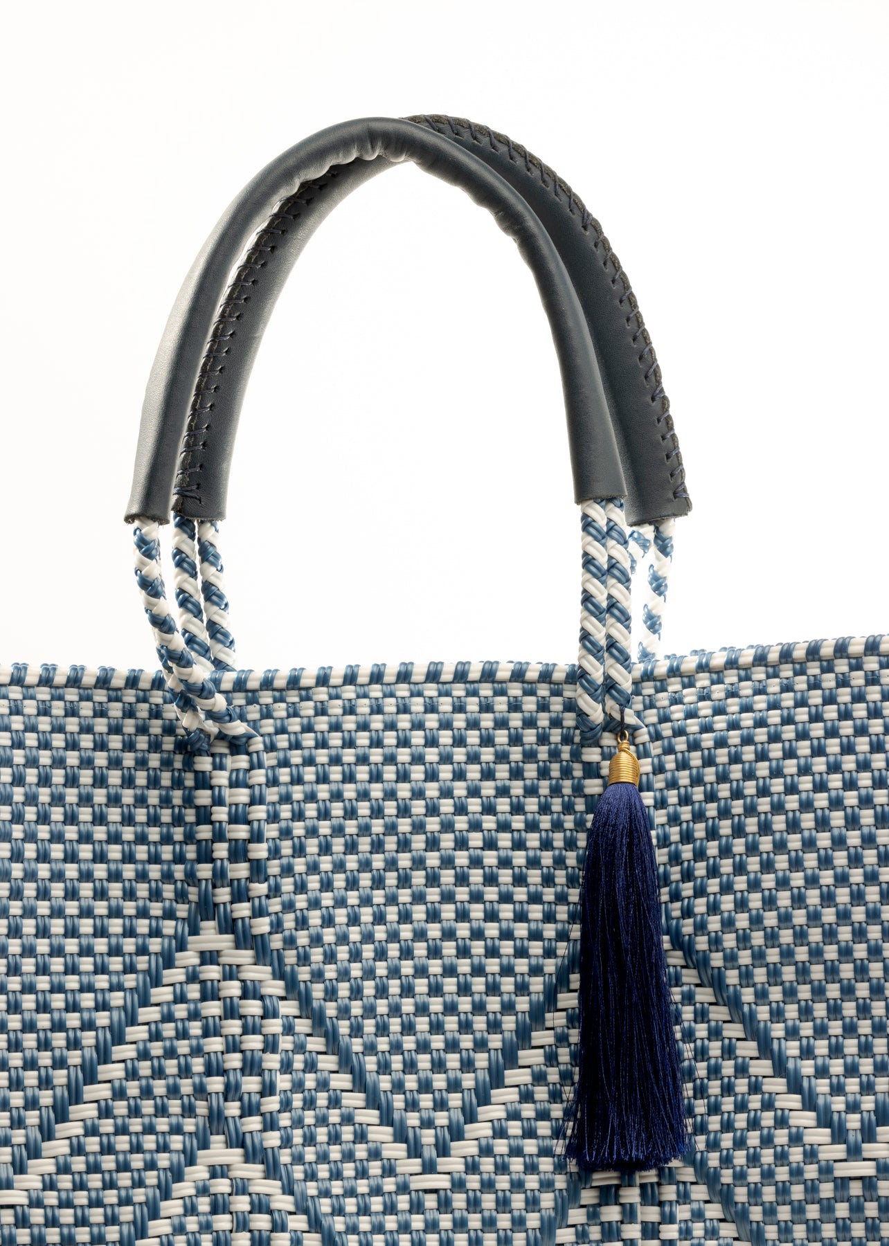 Closeup of fabric of blue and white chevron woven bucket bag made from recycled plastics featuring navy blue leather handles and tassel detail