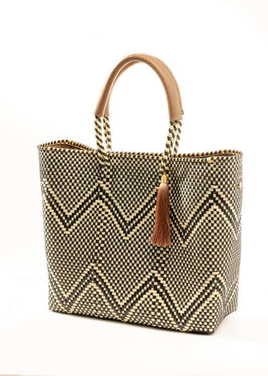Angles view of brown, cream, and tan chevron pattern woven bucket tote made from recycled plastics and featuring tan leather handles and tassel detail